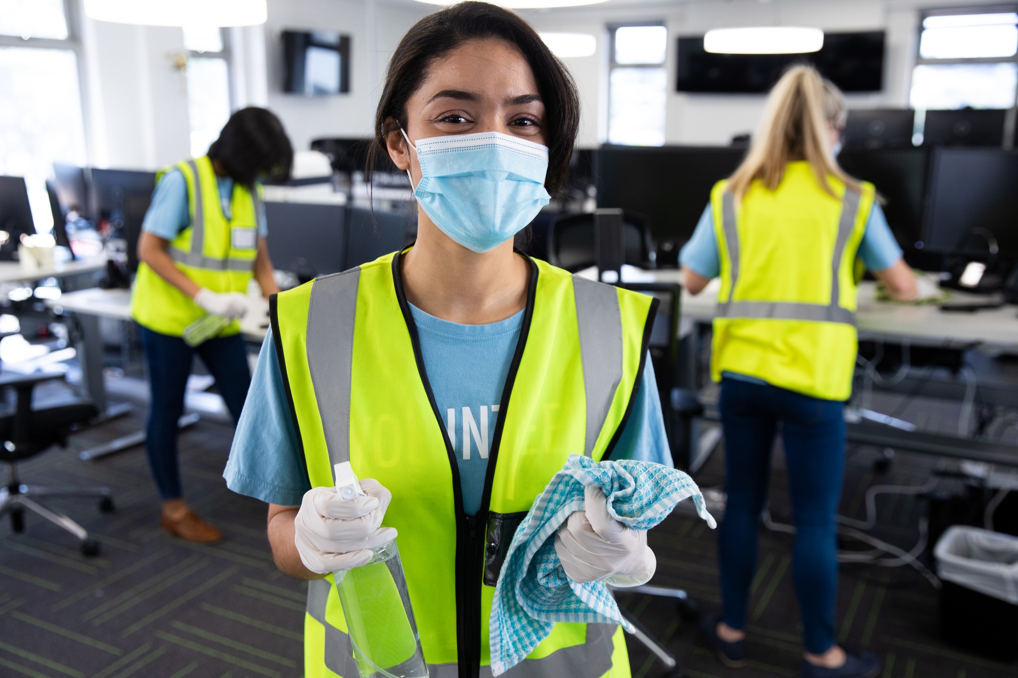 Portrait of woman wearing hi vis vest and face mask holding cleaning cloth and disinfectant